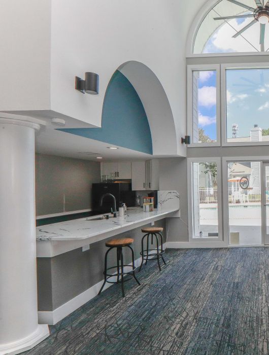 Modern lounge with high ceilings, large windows, bar area, and cozy seating facing a decorative wall and fireplace.