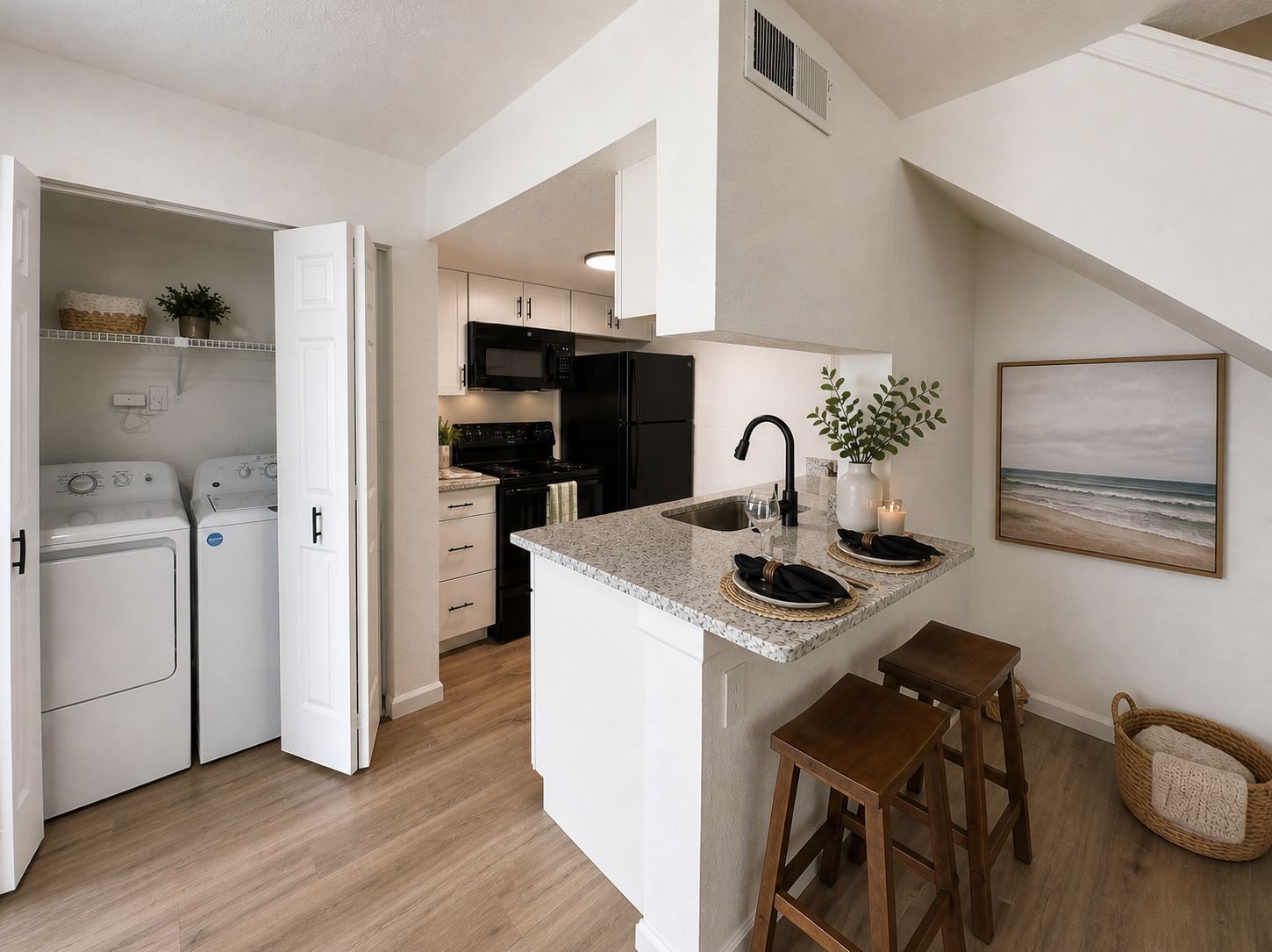 Modern kitchen with a small breakfast bar, two stools, and an open laundry closet with washer and dryer.