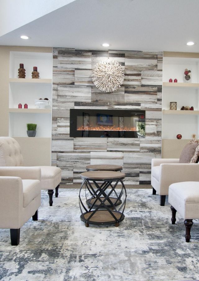 Modern living room with beige chairs, a round coffee table, and a fireplace set in a wood-accented wall.