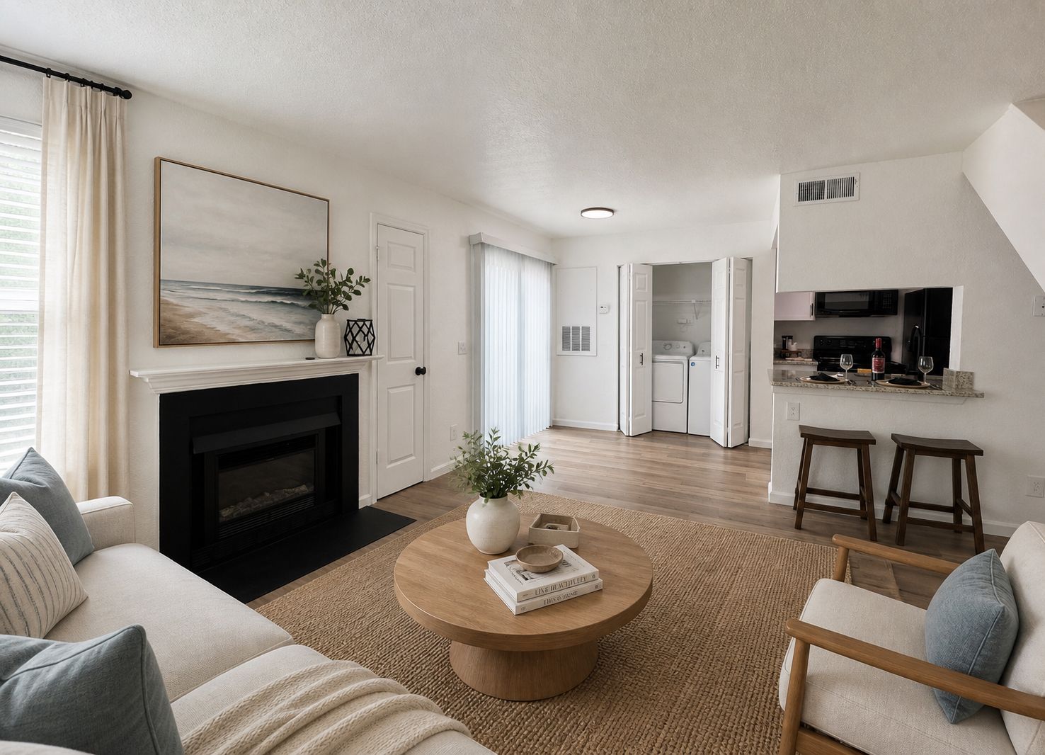 Modern living room with neutral tones, a fireplace, round coffee table, and open view of a laundry area.