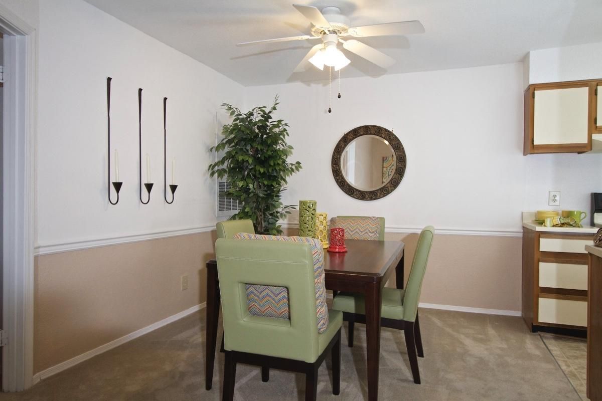 Dining room with a square table, four green chairs, wall decor, a plant, and a round mirror.