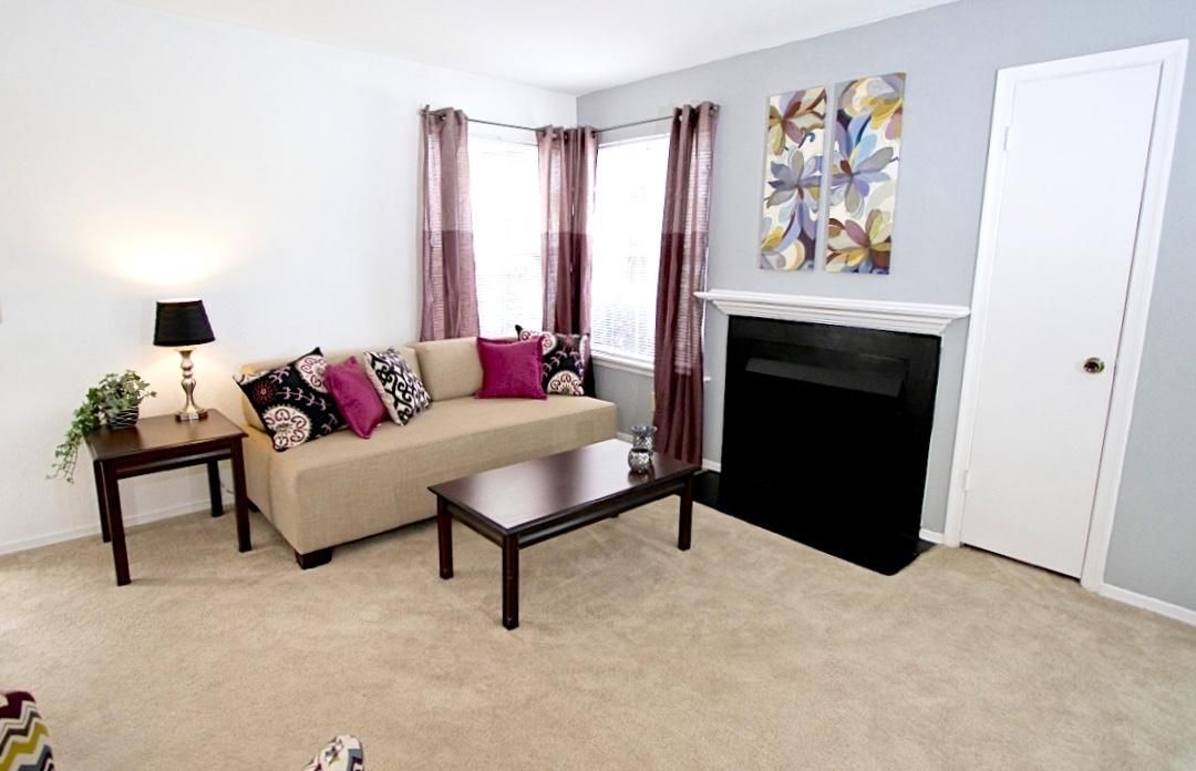 Bright living room with a beige sofa, colorful pillows, coffee table, fireplace, and wall art.
